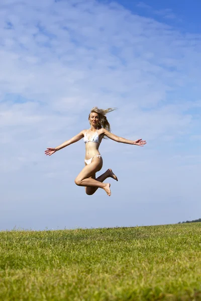 Šťastná žena v bílých bikinách skoky v letní zelené pole proti modré obloze — Stock fotografie