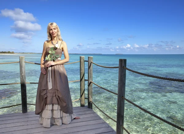 Красивая женщина в длинном платье на деревянной платформе над морем — стоковое фото