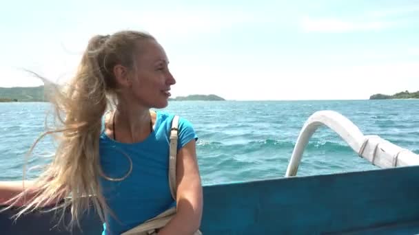 Een jonge slanke vrouw met blond haar vaart op een boot over de zee tussen tropische eilanden — Stockvideo