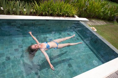 Kadın havuzda su yüzeyinde uzanıyor ve dinleniyor.