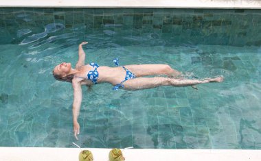 Mutlu, narin genç kadın havuzda bir su yüzeyinde uzanıyor ve dinleniyor.