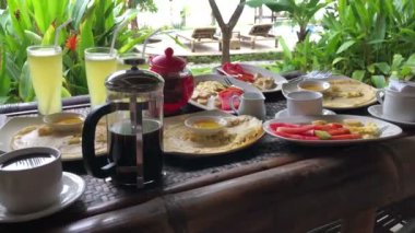 Kahvaltı, gözleme ve meyve, açık terasta sunuluyor, tropikal bitkilere ve bitkilere bakıyor. Endonezya