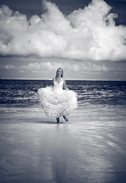 The young beautiful woman in a dress of the bride runs on waves of the sea — Stock Photo, Image
