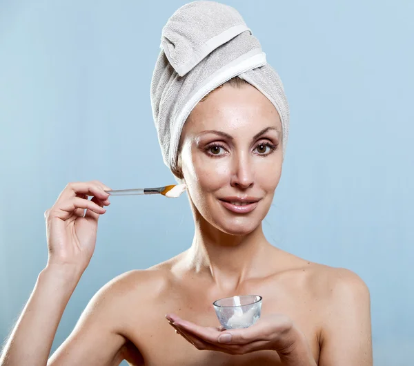 The beautiful woman in a towel puts cream — Stock Photo, Image