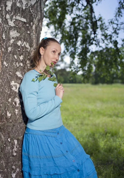 De mooie jonge vrouw in een blauwe jurk in het veld een birc — Stockfoto