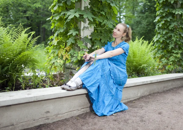 A jovem mulher bonita em um vestido azul no eixo torceu uma bindwee verde — Fotografia de Stock