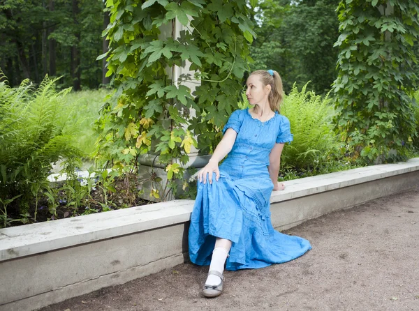 La jeune belle femme dans une robe bleue dans la tonnelle tordu un bindwee vert — Photo