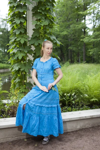 A jovem mulher bonita em um vestido azul no eixo torceu uma bindwee verde — Fotografia de Stock