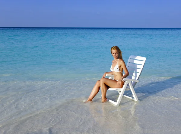 Νεαρή όμορφη γυναίκα σε μια καρέκλα παραλία στη θάλασσα — Φωτογραφία Αρχείου