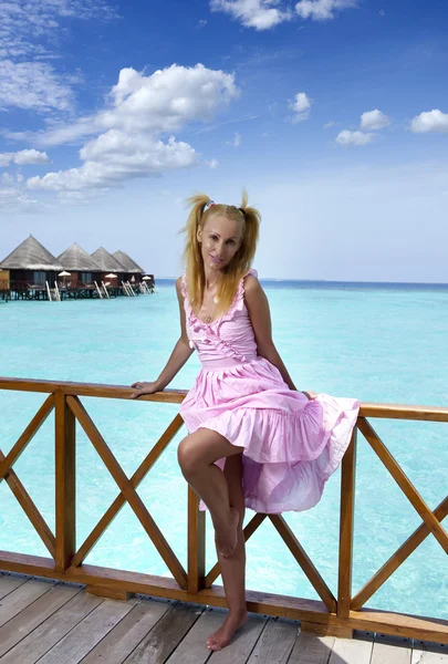 Jovem menina bonita fica em vestido de sol rosa no terraço da villa na água, Maldivas — Fotografia de Stock