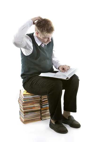 The schoolboy in a school uniform sits on a pack of books, with the opened book in hands — Stock Photo, Image