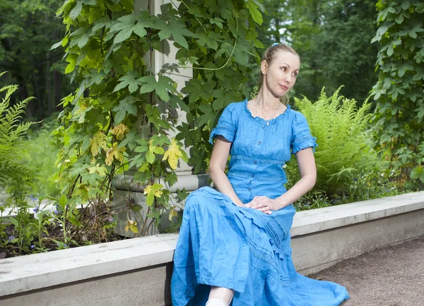 La jeune belle femme dans une robe bleue dans la tonnelle tordu un bindwee vert — Photo