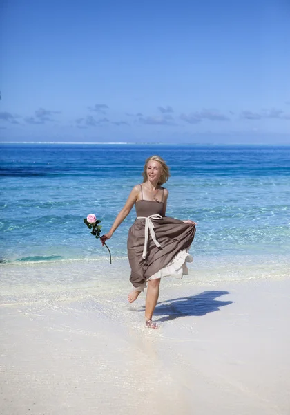 Η όμορφη γυναίκα με ένα τριαντάφυλλο τρέχει στην άκρη της θάλασσας σε μια παραλία. Πολυνησία — Φωτογραφία Αρχείου