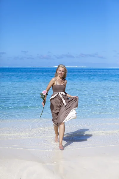 La bella donna con una rosa corre sul bordo del mare su una spiaggia. Polinesia — Foto Stock