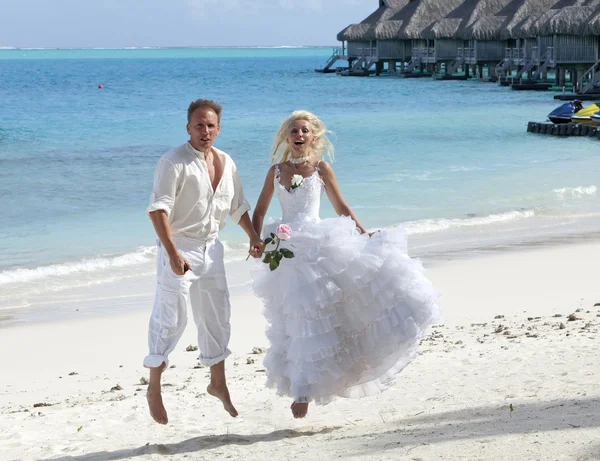 O noivo e a noiva na praia tropical saltam na borda do mar — Fotografia de Stock