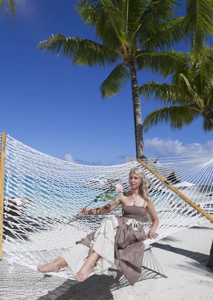 The woman in  long dress with a rose in  hand lies in a hammock on background of the sea — Stock Photo, Image