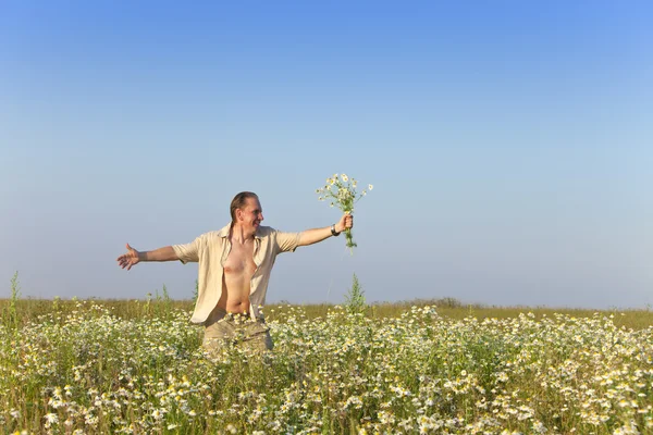 O jovem feliz no campo com um buquê de camomilas — Fotografia de Stock