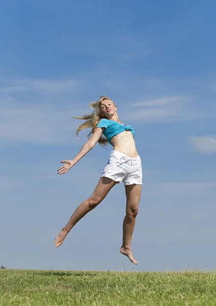 Szczęśliwa kobieta w białym bikini i szorty skacze w lato zielone pole przeciw błękitne niebo — Zdjęcie stockowe