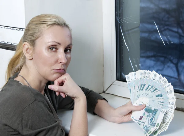 Die traurige junge Frau zählt mit dem geborstenen, zerbrochenen Glas Geld für die Fensterreparatur — Stockfoto