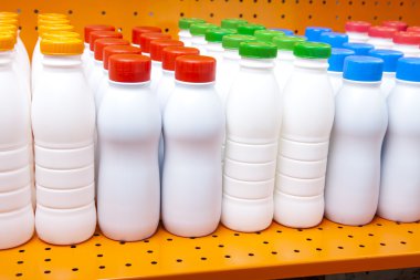 Dükkanda bir rafta parlak kapakları olan süt ve süt ürünleri şişeleri