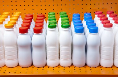 Dükkanda bir rafta parlak kapakları olan süt ve süt ürünleri şişeleri