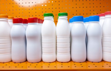 Dükkanda bir rafta parlak kapakları olan süt ve süt ürünleri şişeleri