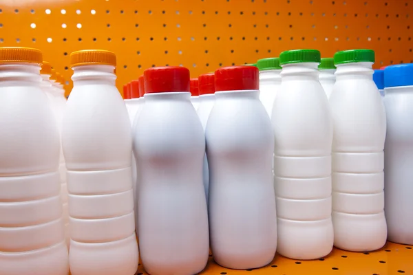 Botellas de productos lácteos con cubiertas brillantes en un estante en la tienda —  Fotos de Stock