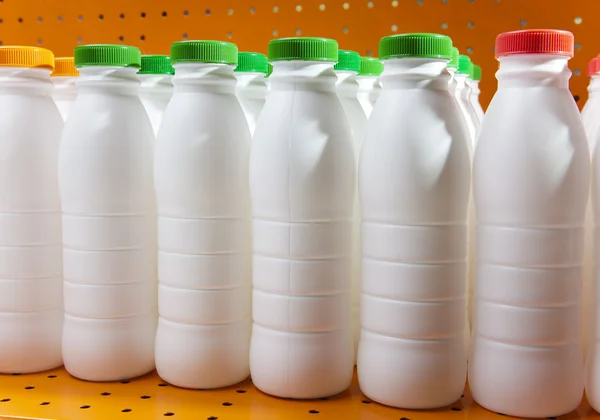 Botellas de productos lácteos con cubiertas brillantes en un estante en la tienda —  Fotos de Stock