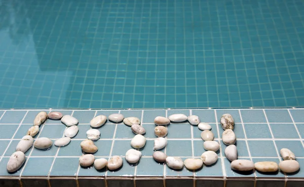 L'inscription "piscine" est disposée par des galets sur le côté de la piscine — Photo