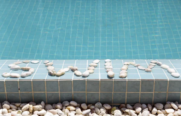 Надпись "Плавать" выложена галькой на стороне бассейна — стоковое фото