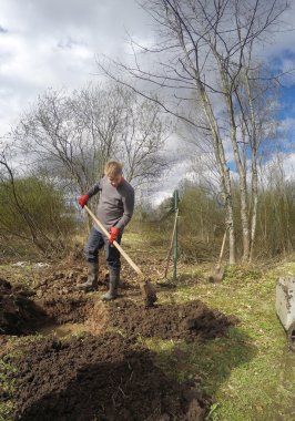 Genç adam zemin kazma ve erken sprin ıslak toprak ekime hazırlanması