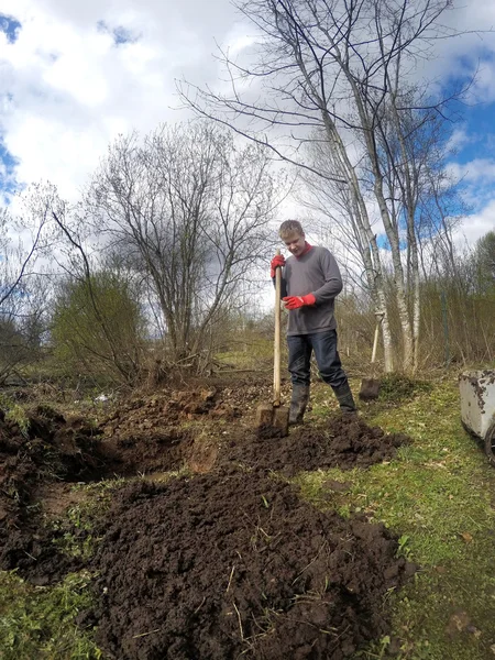 Der junge Mann gräbt Erde um und bereitet sich auf die Pflanzung auf dem nassen Boden im Frühsprinter vor — Stockfoto