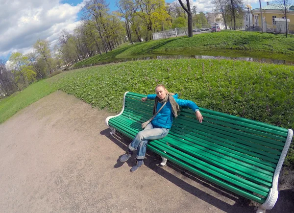 La donna in una giacca azzurra su una panchina in parco nella primavera — Foto Stock