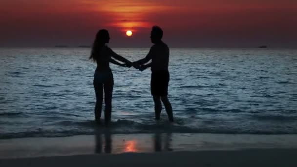 Silhouette of the man and woman, going to the sea on a sunset and kissing in waves — Stock Video