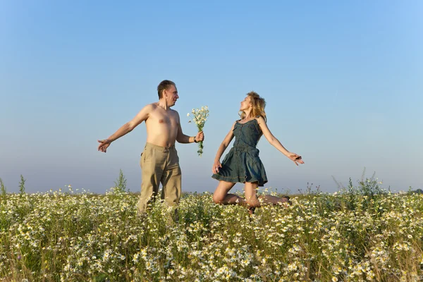 Happy man and the woman jump in the field with camomiles — Stock Photo, Image