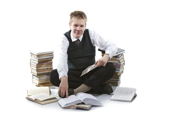 L'écolier en uniforme d'école est assis sur un sol, près de paquets de livres, avec le livre ouvert dans les mains — Photo