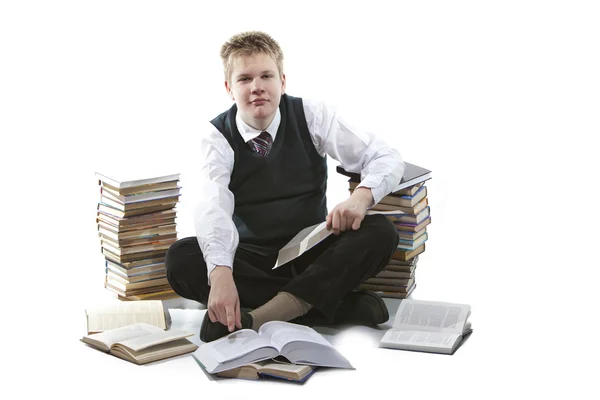 De schooljongen in een schooluniform zit op een vloer, in de buurt van verpakkingen van boeken, met het geopende boek in handen — Stockfoto