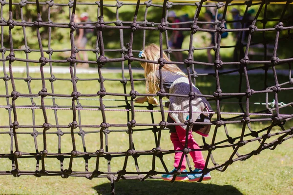 Niña yendo a través de la red de cuerda en el parque — Foto de Stock