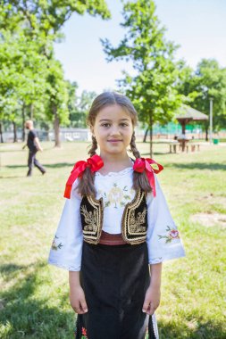 Serbian folklore, smiling cute little girl in traditional Serbian clothing. Outdoor portrait, summer day. 