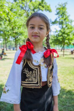 Serbian folklore, smiling cute little girl in traditional Serbian clothing. Outdoor portrait, summer day. 
