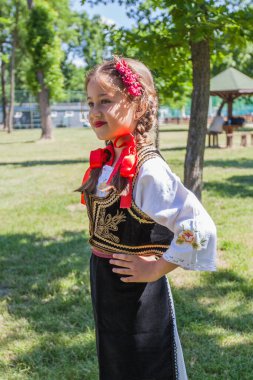 Serbian folklore, smiling cute little girl in traditional Serbian clothing. Outdoor portrait, summer day. 
