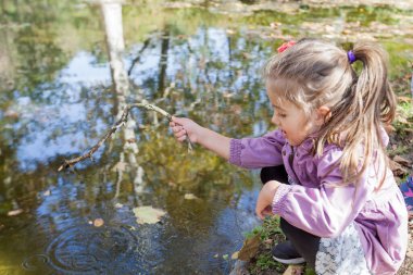 Two little girls playing in park near lake. Reflection of trees on water. Autumn sunny day.