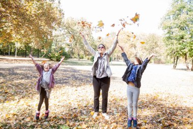 Happy family enjoying sunny autumn day in the park. Mother with two daughters outdoor.