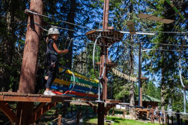 Macera parkında güvenlik ekipmanı içinde küçük bir kız. Çocuk dışarıda eğleniyor. Çocukluk sporları ekstrem aktiviteler. Yaz ışığı.