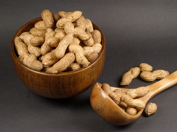 Un cuenco de madera de cerezo y cuchara de cacahuetes sobre un fondo negro . — Foto de Stock