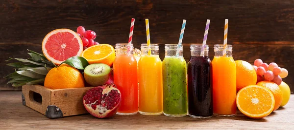 bottles of fruit juice with fresh fruits on a wooden table