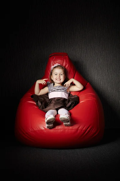 Little girl sitting on red beanbag — Stock Photo, Image