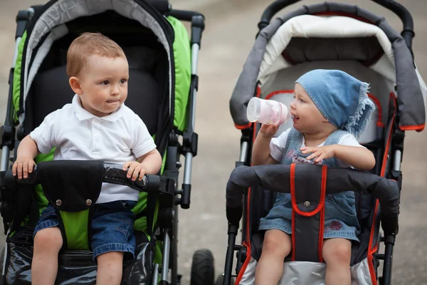 Cute baby drinks juice sitting in baby carriage — Stock Photo, Image