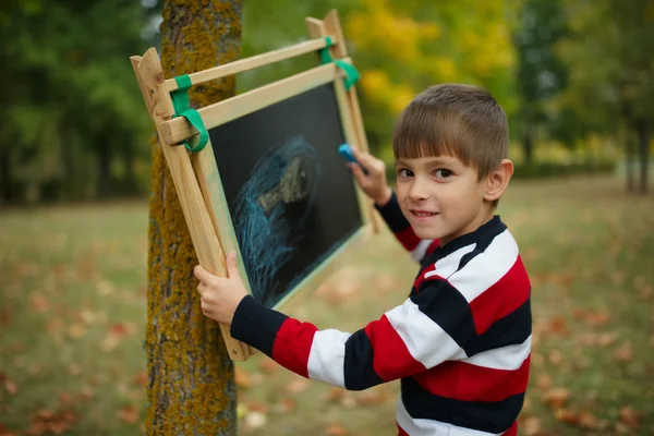 Маленький щасливий хлопчик пише на дошці — стокове фото
