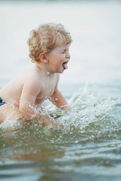 Liten rolig pojke spelar i vatten — Stockfoto